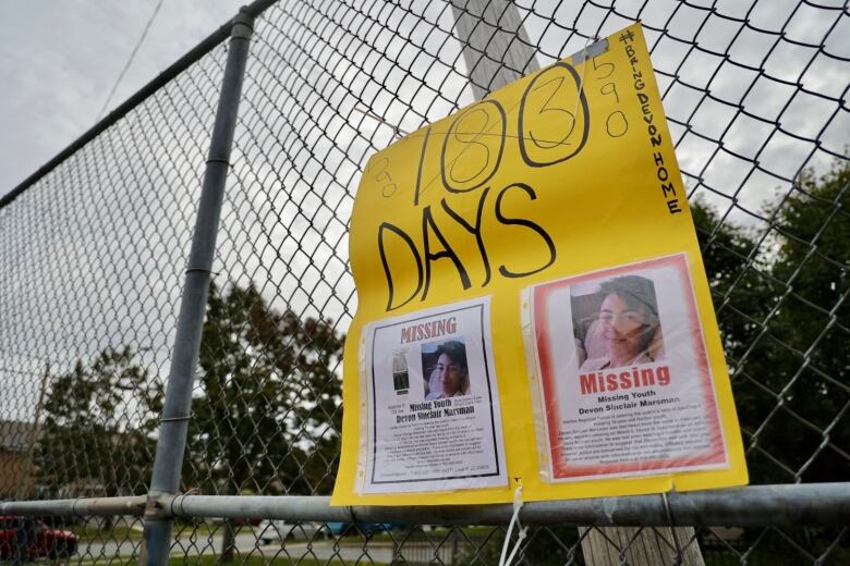 A sign with pictures of Devon on it hangs on a fence. 