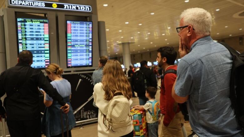 Travellers look at electronic departure signs at an airport.