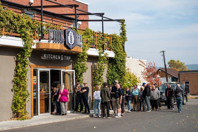 A group of dozens of people line up outside a restaurant. 