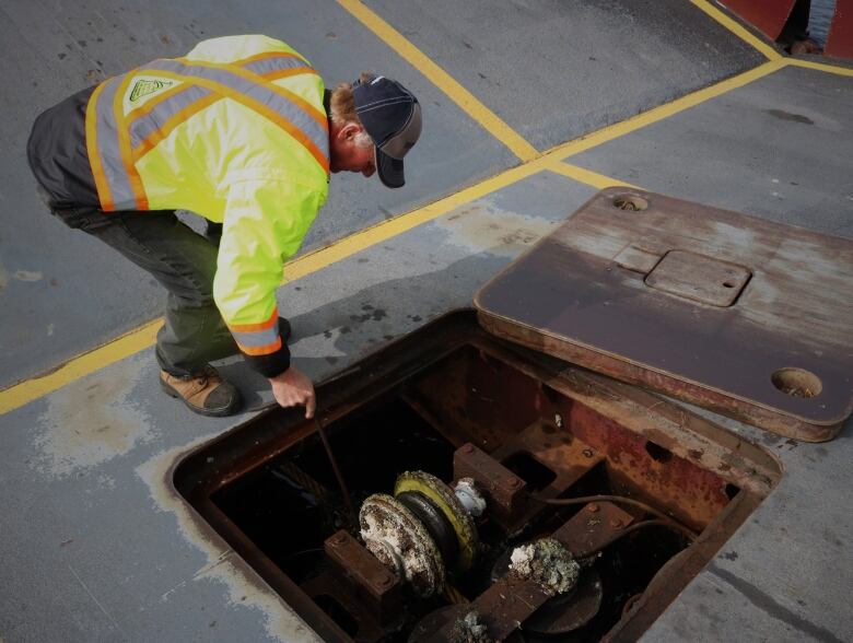 A man leans over a hatch on the cable ferry which has been opened to reveal the cable mechanism that drives the boat. 