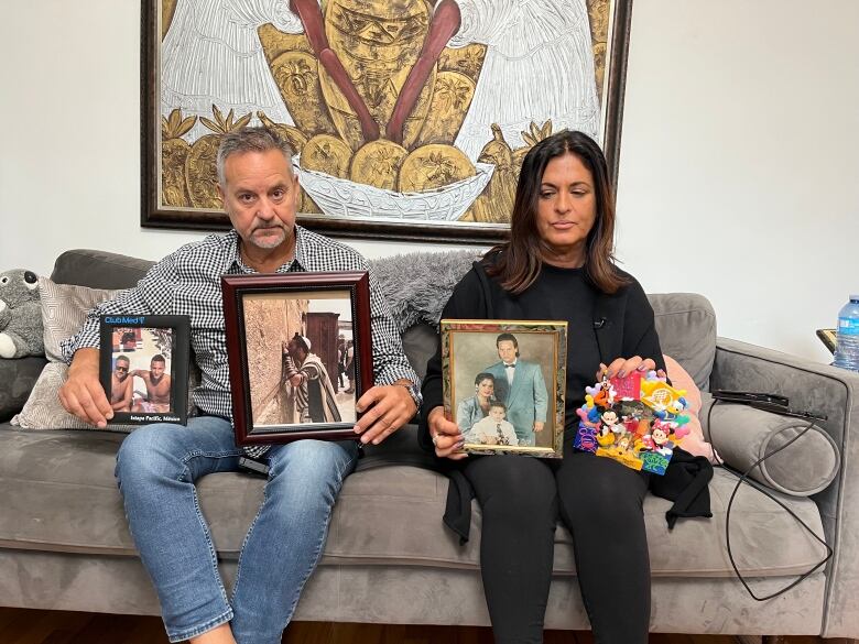 Two distraught parents sit on a couch holding photos of their dead son. 