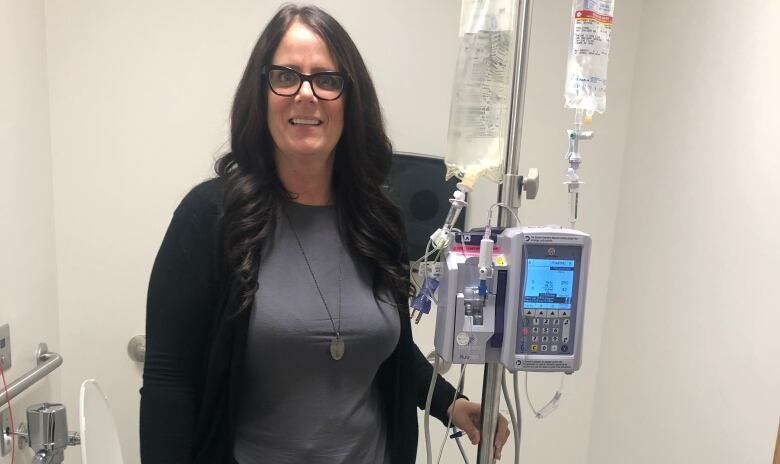 A woman in a grey shirt and black pants can be seen standing in a hospital, holding a machine. 