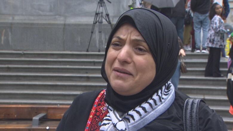 A woman in a hijab and a traditional scarf cries at a protest.