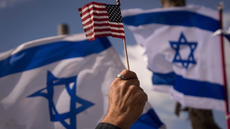 Hand holds U.S. flag in front of Israeli flags