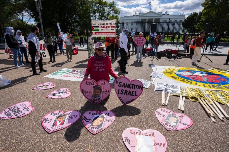 Protesters in front of White House hold signs including many shaped like hearts, with phrases like, 