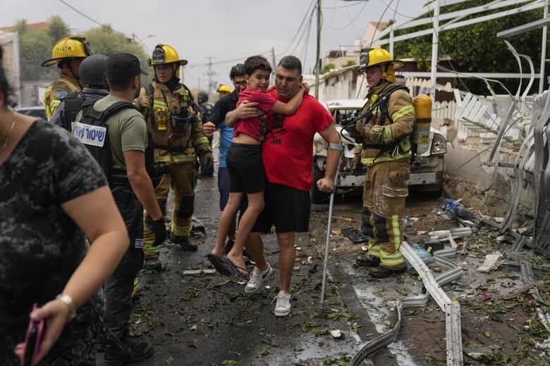 A man carries a distraught boy through rubble and rescue workers.