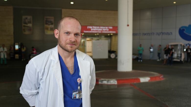 A man in scrubs and a doctor's jacket stands in a hospital emergency bay.