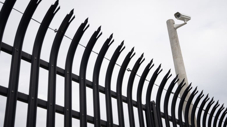 A security camera over a tall, black, pointed metal fence.