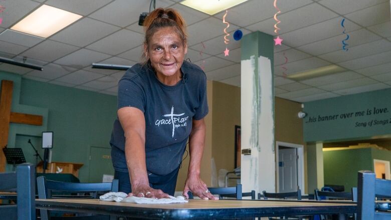 A woman wipes a table clean with a smile on her face.