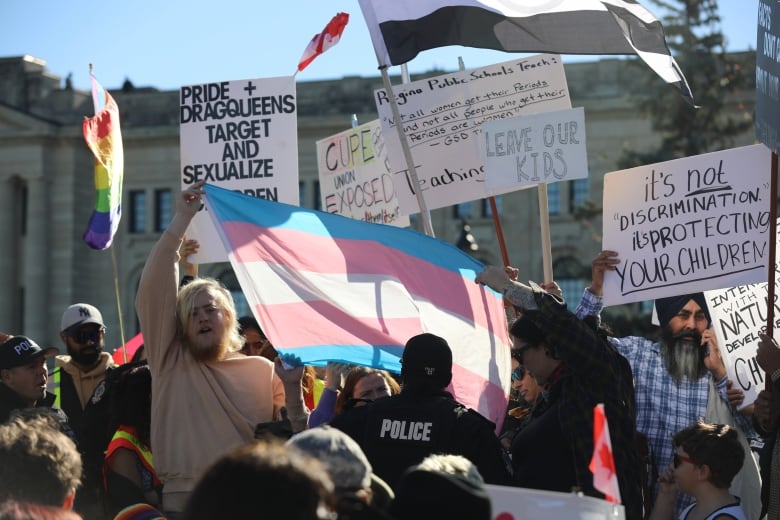 A police officer speaks with people holding a transgender flag in front of protestors in favour of the Saskatchewan government's pronoun policy. 