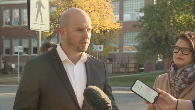 Matt Love is speaking into a microphone with Carla Beck standing behind him