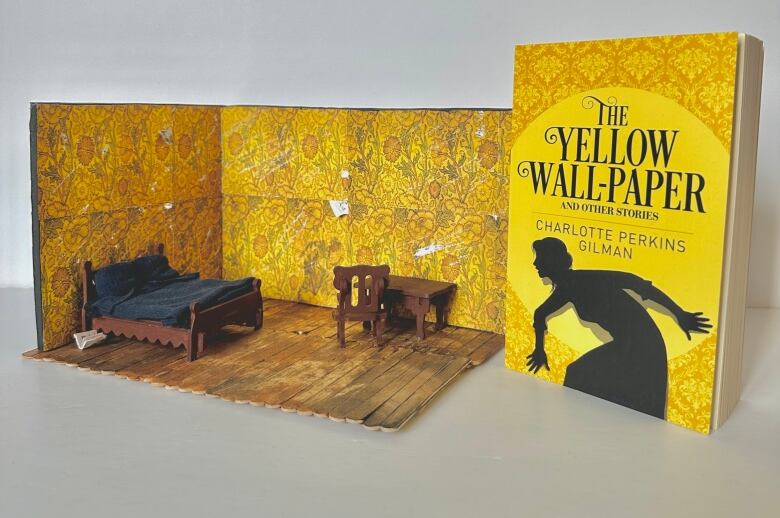 A miniature space, showing a small bed and desk in a room with bright patterned yellow wallpaper. A book with the title The Yellow Wall Paper sits to the right of the room.