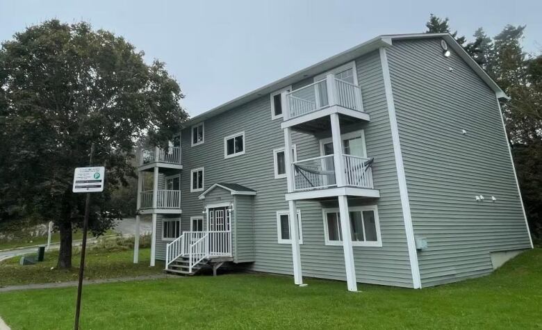 A grey apartment building with white fixtures on a short-cut green lawn.