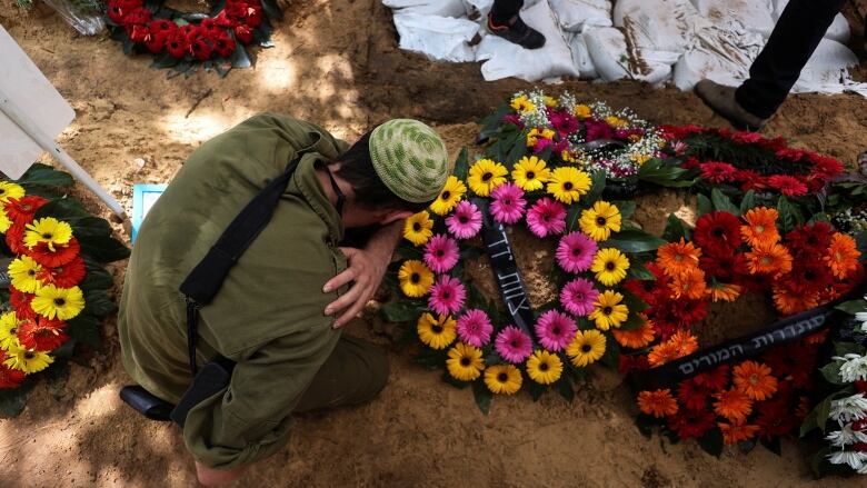 A man kneels at a grave with flowers on top of it