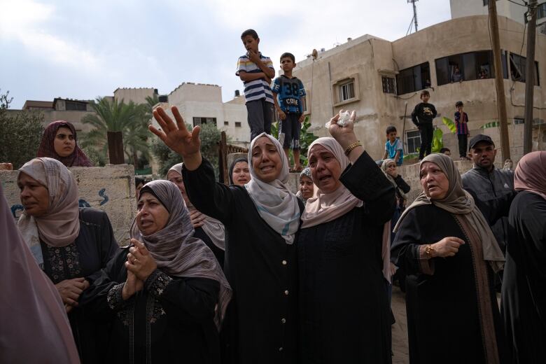 A group of people, mostly women and children, look distraught. 