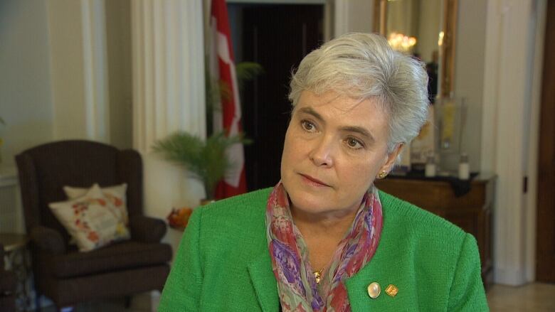 A woman with grey hair wears a green leather jacket and looks off camera. 