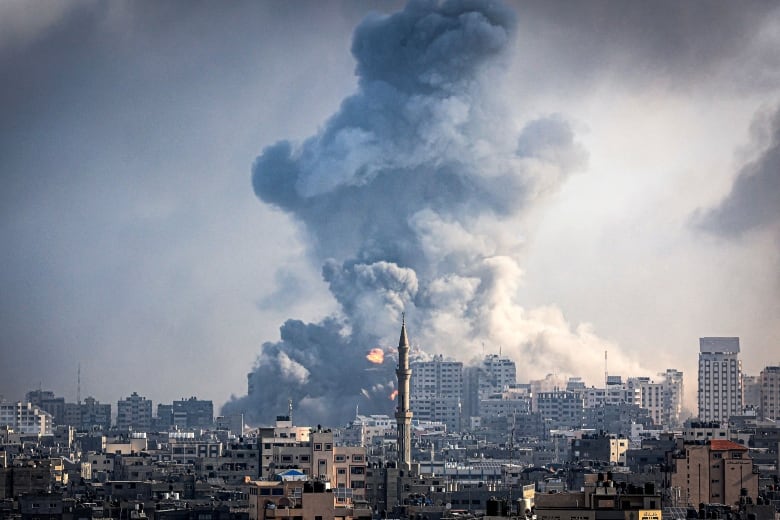 A huge grey smoke cloud looms over a crowded skyline with a minaret in its centre.