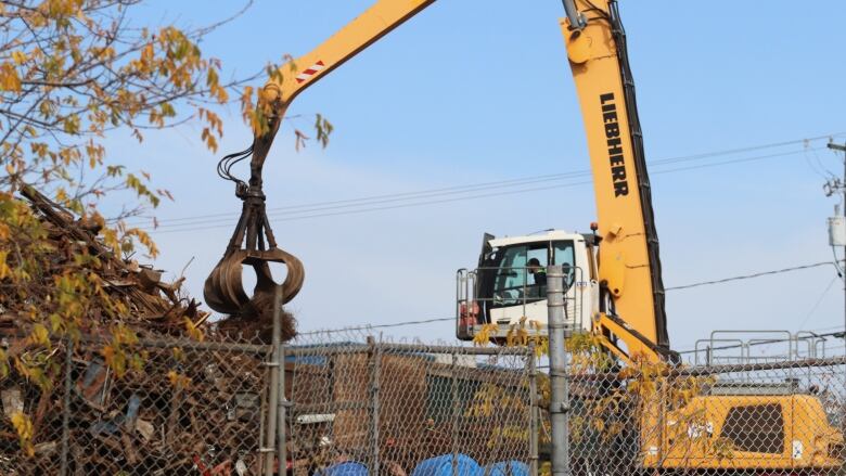 A yellow machine with a claw at the end of a large boom lifting scrap material. 