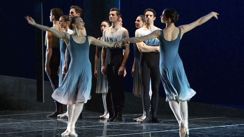 Two ballet dancers dance on a stage while others watch from backstage. 