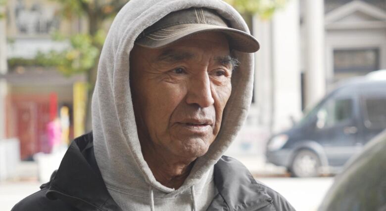 Charles Morrison is a residential school survivor who lived for several years in Vancouver's Downtown Eastside. He is wearing a grey sweater, black jacket and brown baseball cap. 