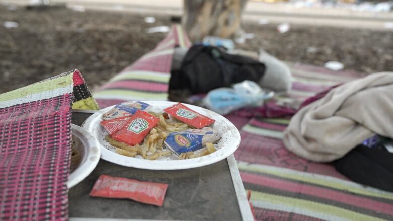 An abandoned plate of french fries and ketchup packets next to a mat  with blankets.