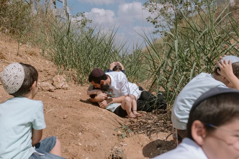 People in yarmulkes are shown on the ground outside, with a man covering a small child.