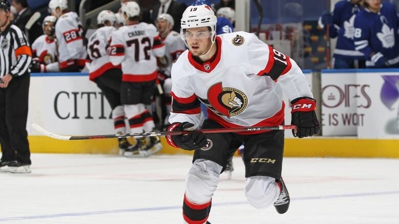 A hockey player wearing a white, red and black Ottawa Senators jersey skates on the ice during a game.