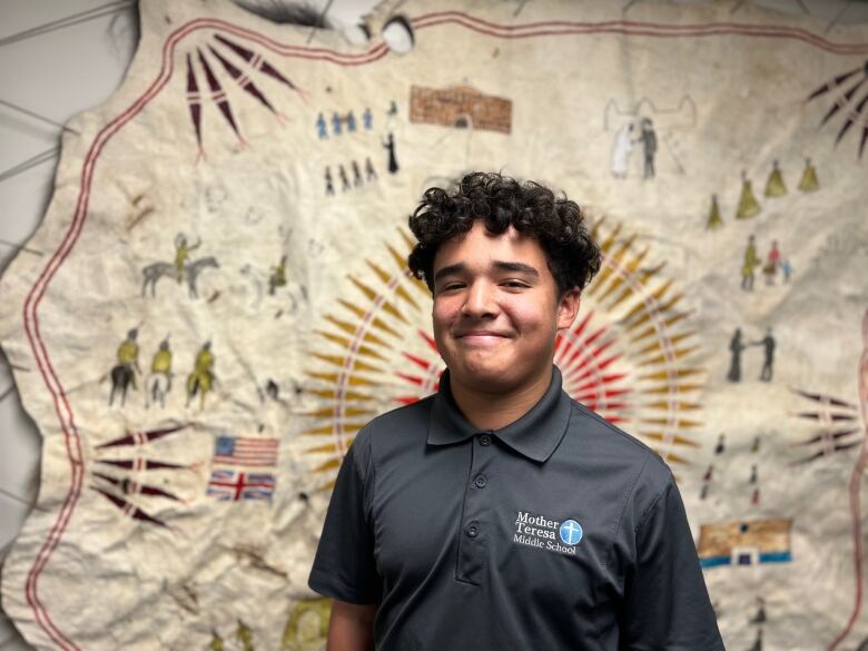 a young person is wearing a dark shirt in front of a colorful blanket on the wall.