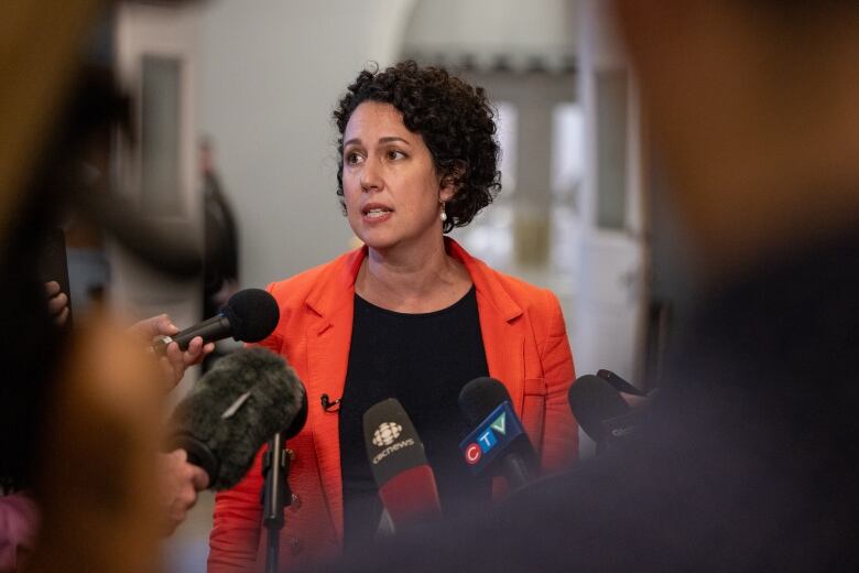 A woman stands in front of microphones.