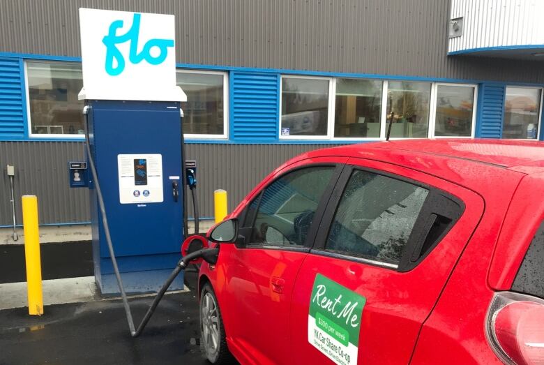 A small red car plugged into an electric vehicle charging station.