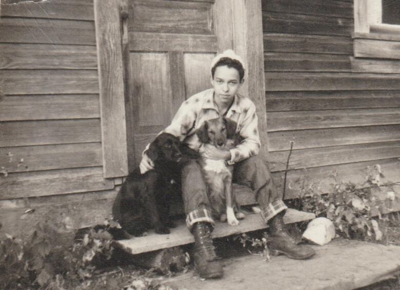 In a black and white photo, a boy is shown sitting on a front step with a dog in his lap.