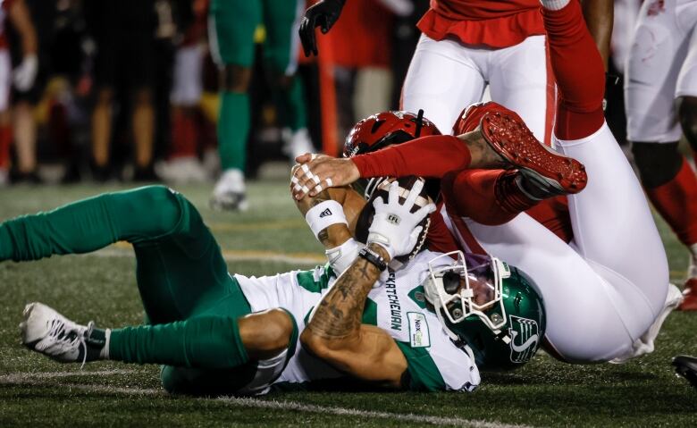 Roughriders wide receiver Kian Schaffer-Baker hangs on to the ball on the ground as he is tackled by Calgary Stampeders linebacker Cameron Judge