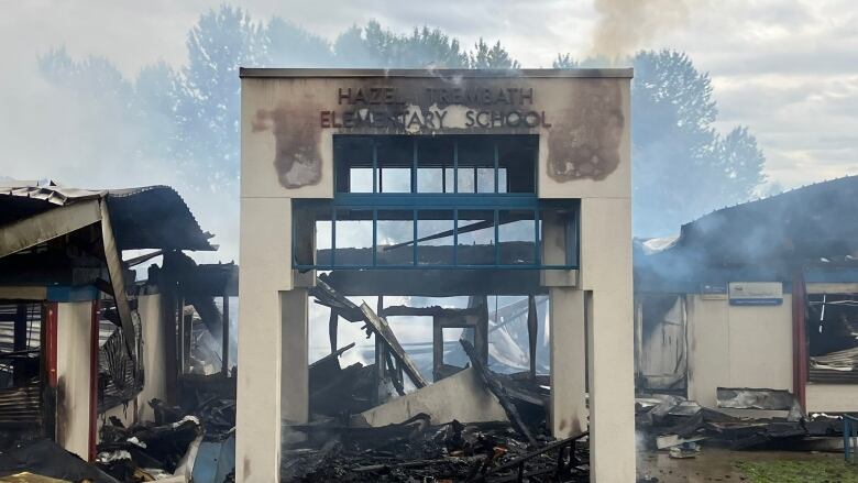 A school entrance stands among the smouldering, smoking ruins of a fire.