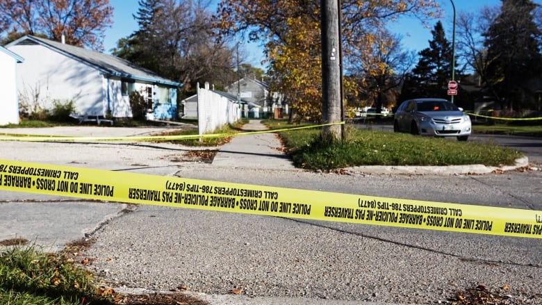 Yellow police tape is attached to a pole next to a side walk.