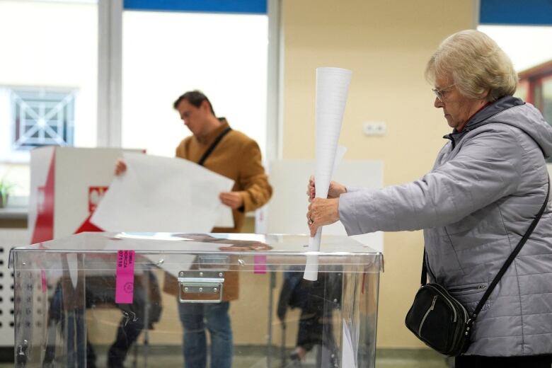 A voter casts a large paper ballot into a clear box.