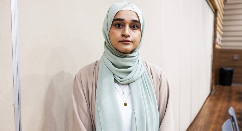 A young woman wearing a hijab is pictured looking towards the camera.