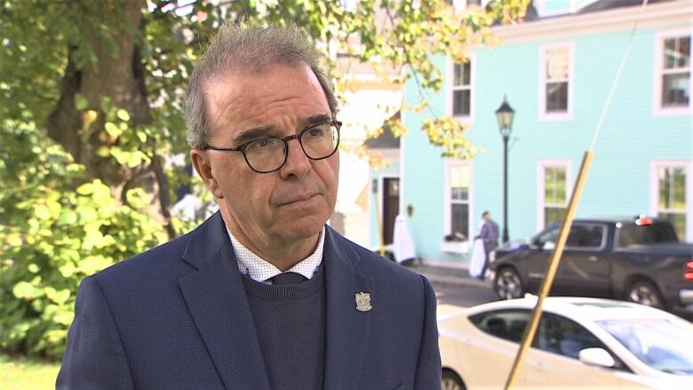 Philip Brown outside in sweater and jacket with green leaves in background.