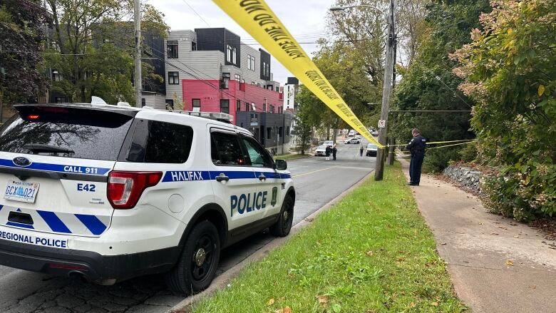 Yellow police tape and a white and blue police vehicle are shown on a street.