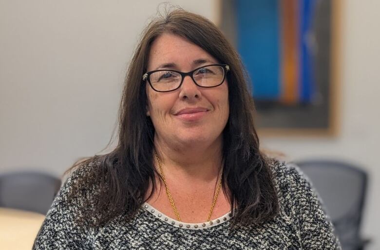 A woman in a grey sweater and glasses in a boardroom 