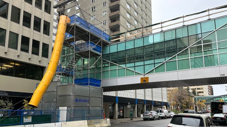 Scaffolding is built next to an indoor, overhead pedway straddling a downtown street.