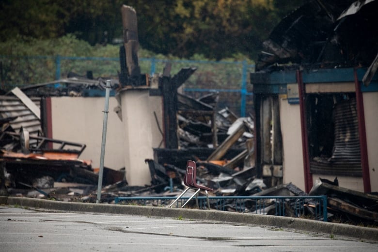 A solitary chair lies on a pavement near a destroyed building.