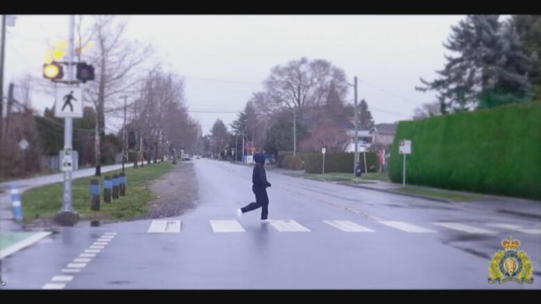 A woman in dark clothes crosses a street at a crosswalk.