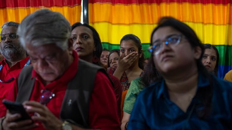 A person sitting in a crowd holds their hand over their mouth in dismay.