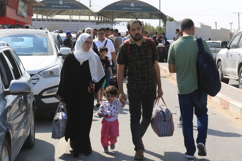 A couple and their child walk by another man, with people following behind them at the Rafah border crossing.