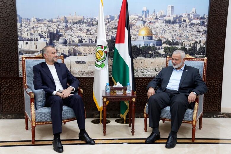 Two men sit in chairs with flags propped between them.