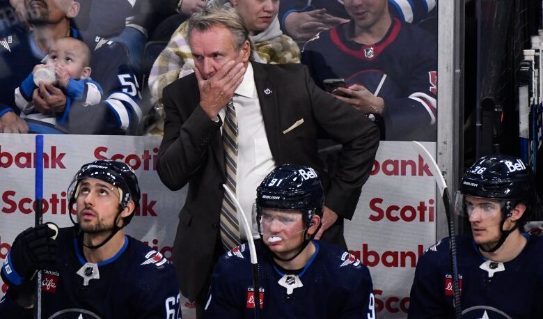 The coach of a hockey team stands behind players who are sitting on a bench.