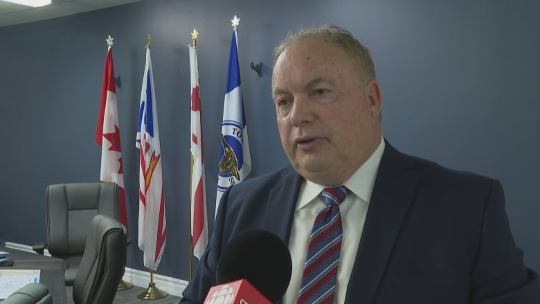 A man wearing a striped tie looks to the left as he speaks into a camera.