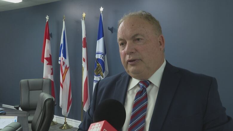 A man wearing a striped tie looks to the left as he speaks into a camera.