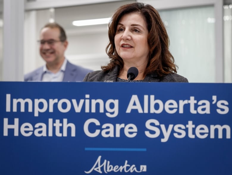 A woman is pictured behind a sign that reads 'Improving Alberta's Health Care System.'