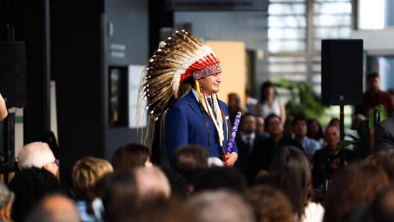 A man wearing a headdress stands among a crowd of people.